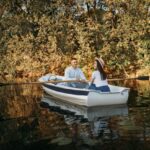Love couple boating on lake, water reflection
