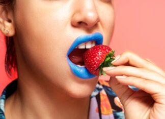 Kameleon Close-up portrait of a woman with blue lipstick holding a fresh strawberry.