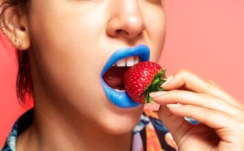 Kameleon Close-up portrait of a woman with blue lipstick holding a fresh strawberry.